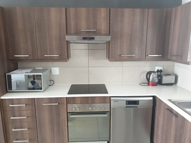 Modern kitchen featuring wood-grain cabinetry, stone countertops, tiled backsplash, and integrated stainless steel appliances including an oven, hob, and dishwasher.