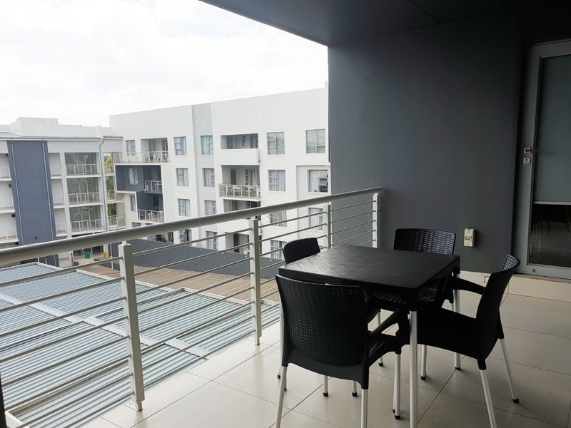 A covered balcony featuring tiled flooring and a metal balustrade, offering an elevated view of the surrounding apartment complex.