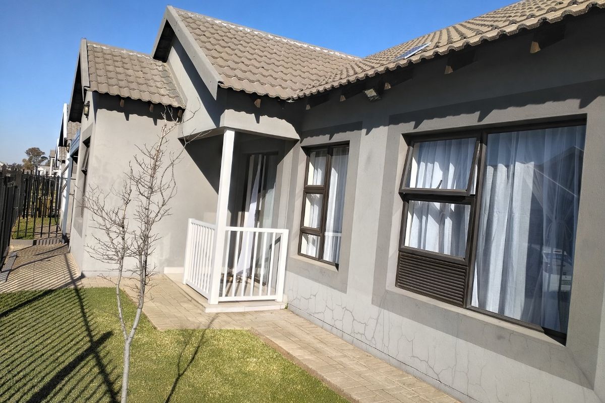 Rear exterior view of the townhouse featuring a paved walkway, concrete tiled roof, and aluminium window frames with visible plaster cracking.