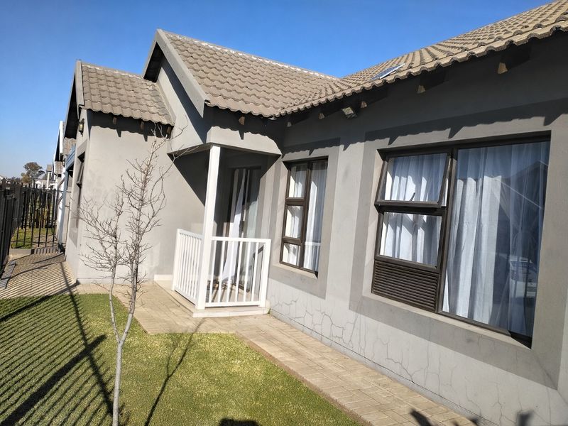 Rear exterior view of the townhouse featuring a paved walkway, concrete tiled roof, and aluminium window frames with visible plaster cracking.