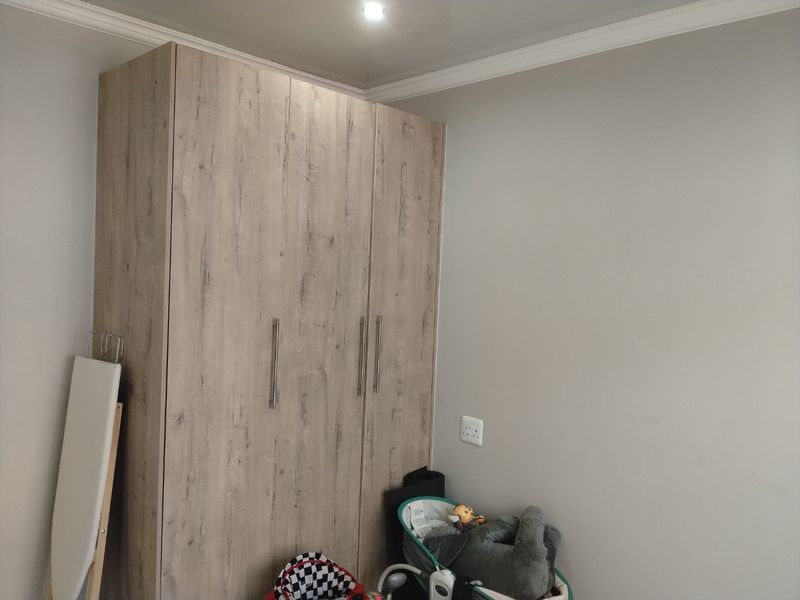 A bedroom featuring a modern wood-grain finish built-in wardrobe, neutral wall paint, and decorative ceiling coving.