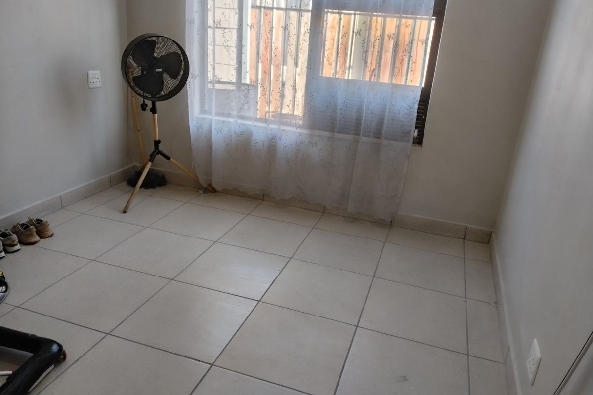A simple, empty bedroom featuring neutral tiled flooring and a window fitted with security bars, offering a clean canvas for personalization.