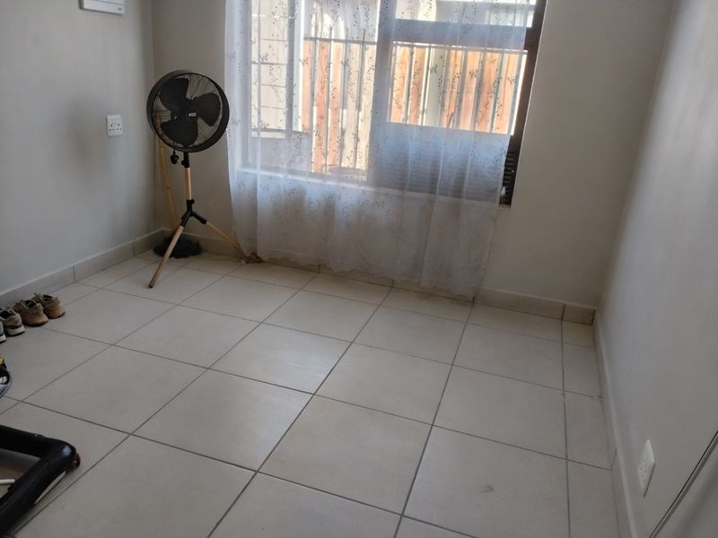 A simple, empty bedroom featuring neutral tiled flooring and a window fitted with security bars, offering a clean canvas for personalization.
