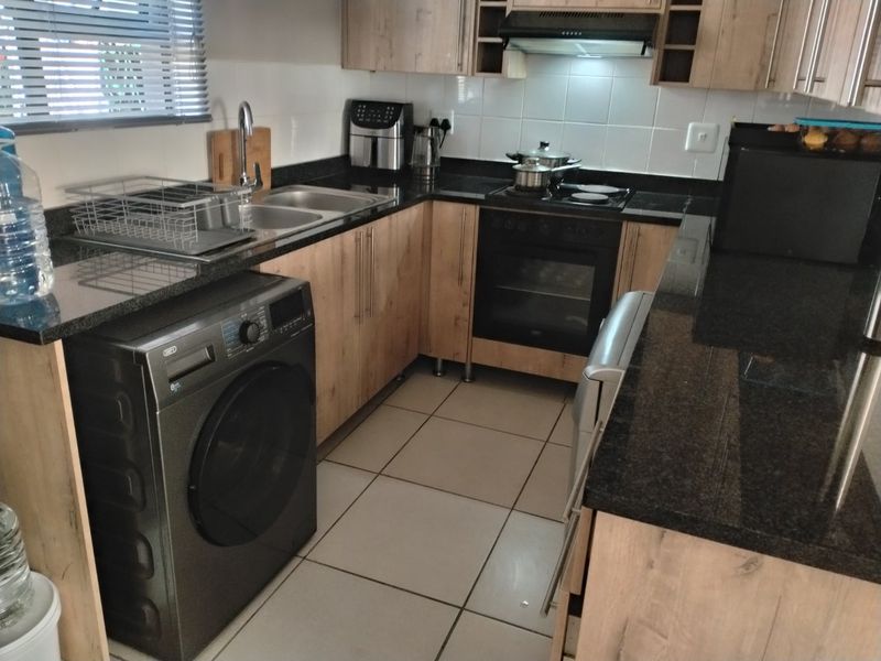 A functional kitchen featuring laminate cabinetry, granite countertops, built-in oven, electric hob, extractor fan, and tiled flooring.