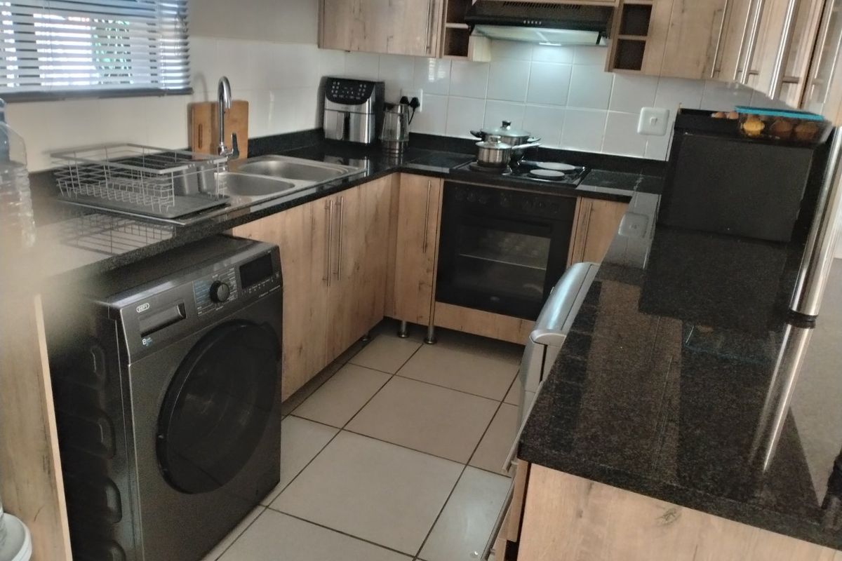 Functional kitchen featuring light wood-look cabinetry, dark granite countertops, built-in oven, electric hob, and tiled flooring with a practical layout.