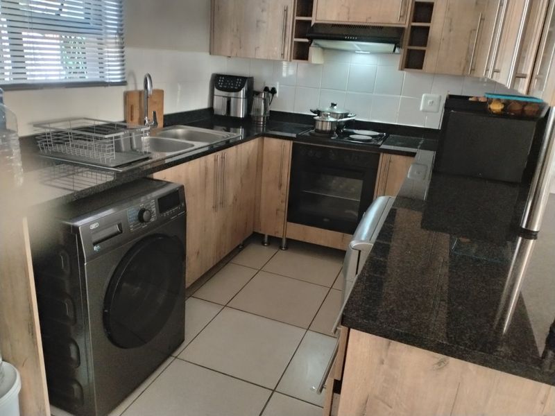 Functional kitchen featuring light wood-look cabinetry, dark granite countertops, built-in oven, electric hob, and tiled flooring with a practical layout.