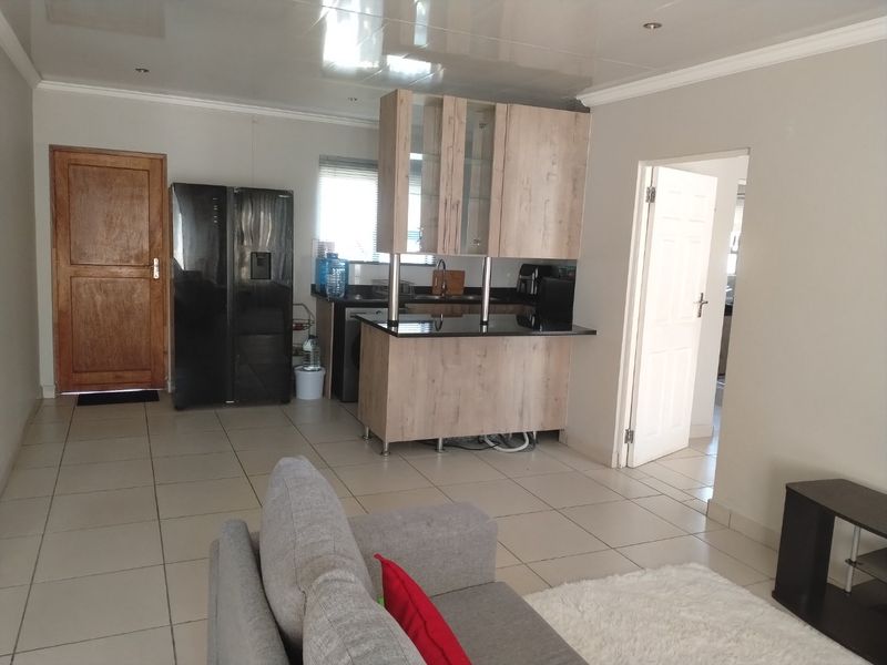 Open plan living area featuring a compact kitchen with wood-look cabinetry, granite countertops, and tiled flooring throughout.