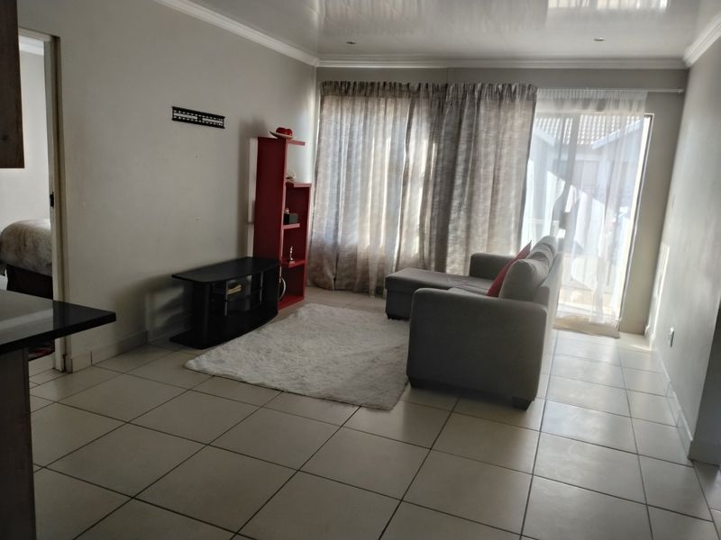 A bright living room featuring tiled flooring, coved ceilings, and a sliding glass door providing access to the exterior.