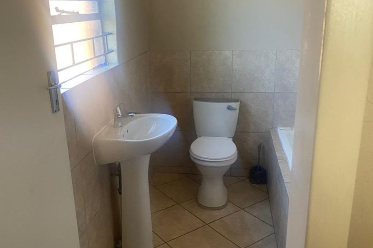 A functional bathroom featuring a pedestal basin, toilet, and bathtub with neutral floor and wall tiling.