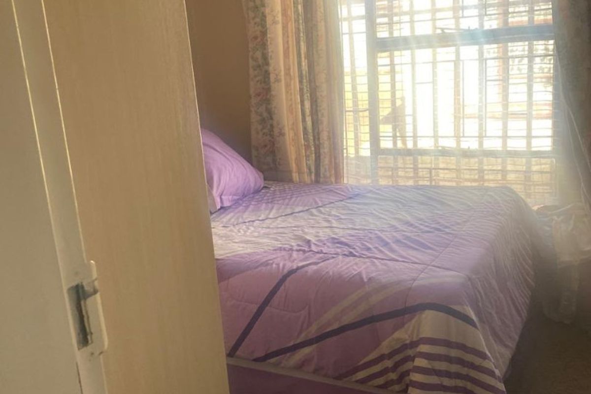 A bedroom featuring a window with installed security bars, allowing natural light into the space.