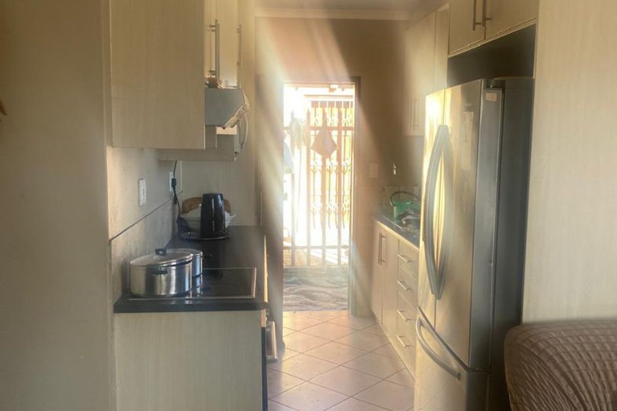 A galley-style kitchen featuring built-in cabinetry, tiled flooring, and a cooktop, leading directly to an exterior doorway.