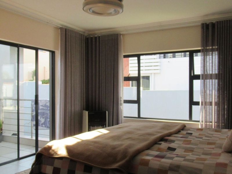 A well-lit bedroom featuring large aluminium-framed windows and a sliding glass door providing access to an outdoor balcony area.