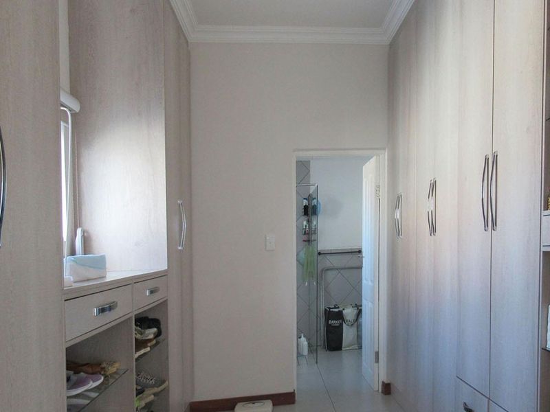 A walk-in dressing area featuring extensive built-in cabinetry with light wood-grain finish and tiled flooring, leading through to an adjacent bathroom.