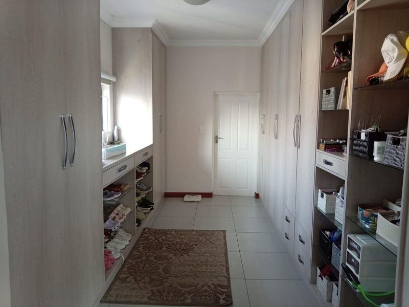 A well-organized walk-in closet or dressing area featuring extensive built-in cabinetry with light wood-grain finish and neutral tiled flooring.