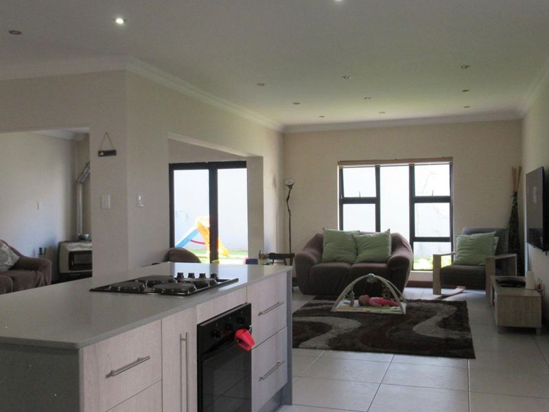 Spacious open-plan living area featuring a modern kitchen island with built-in hob and oven, tiled floors, and seamless flow to the outdoor patio area.
