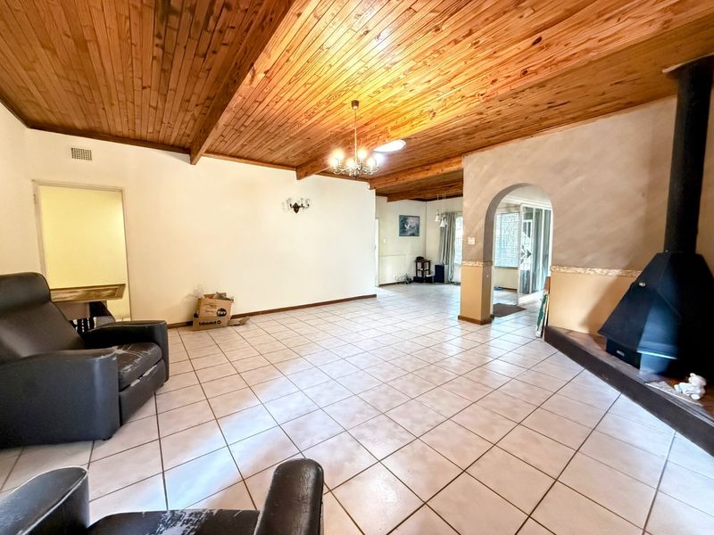 Spacious living area featuring a vaulted timber-clad ceiling, tiled flooring, and a prominent freestanding fireplace, with an arched transition to adjacent living spaces.