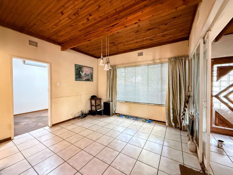 A spacious living area featuring a timber-clad ceiling, ceramic floor tiles, and direct access to the exterior through a sliding glass door.
