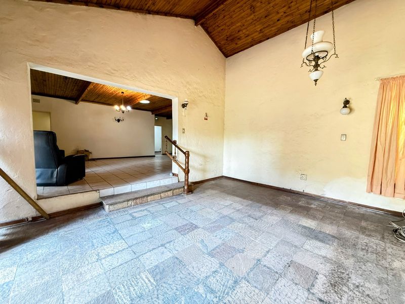 Spacious split-level living area featuring a vaulted timber ceiling, stone tile flooring, and characterful architectural details, offering a blank canvas for renovation.