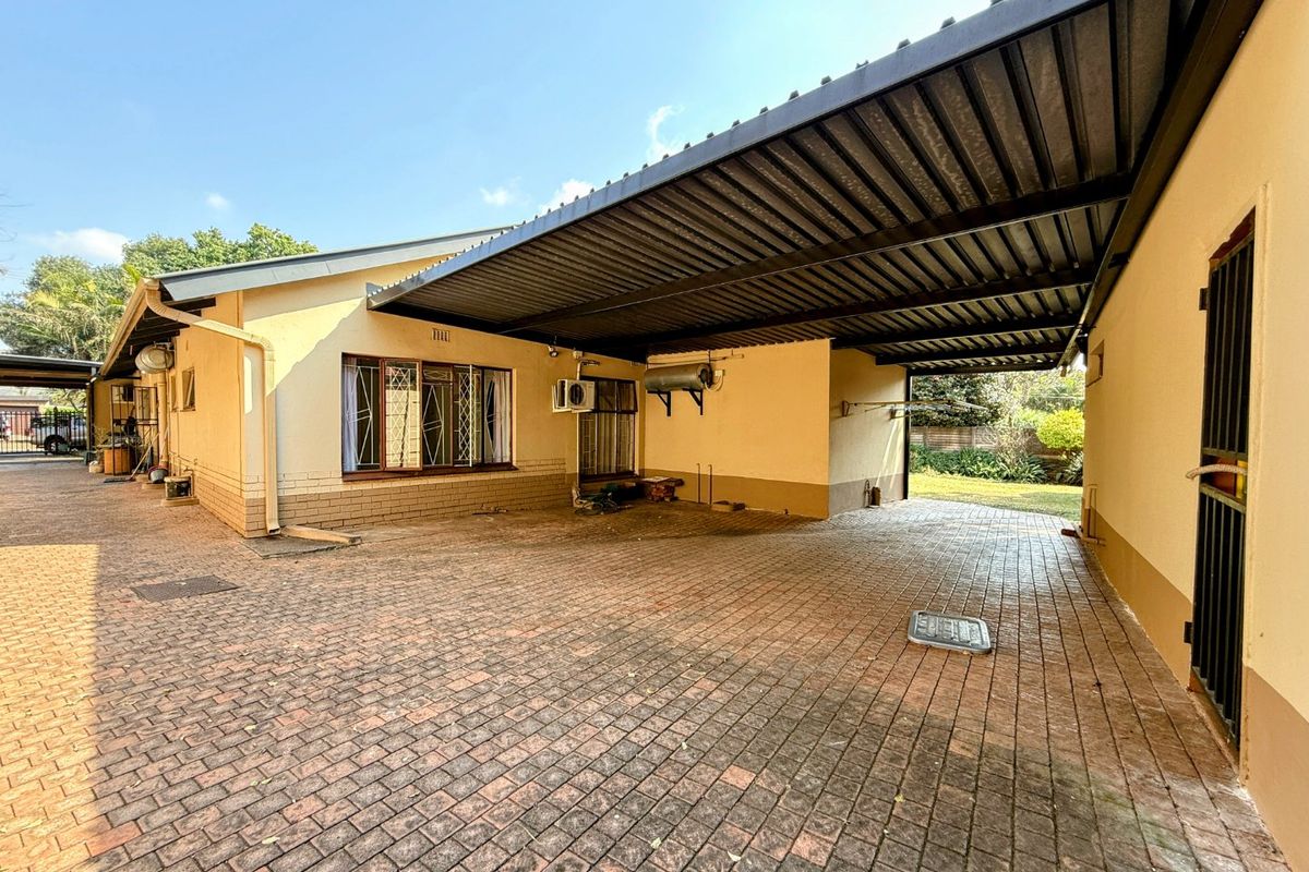 A spacious paved rear courtyard featuring a large covered carport, security gates, and external utility fixtures.
