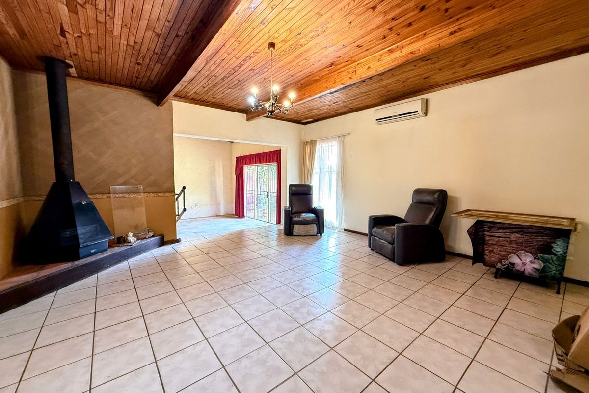Spacious living room featuring a high exposed timber beam ceiling, tiled flooring, and a prominent freestanding fireplace, with access to an adjoining area.