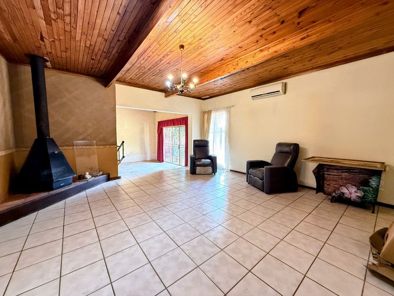 Spacious living room featuring a high exposed timber beam ceiling, tiled flooring, and a prominent freestanding fireplace, with access to an adjoining area.