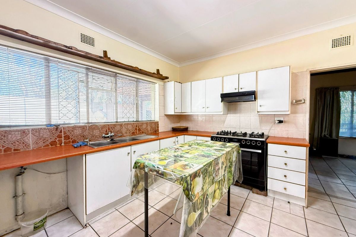 A functional kitchen featuring white cabinetry, tiled splashbacks, a double sink, and a freestanding stove, offering potential for modernization and cosmetic updates.