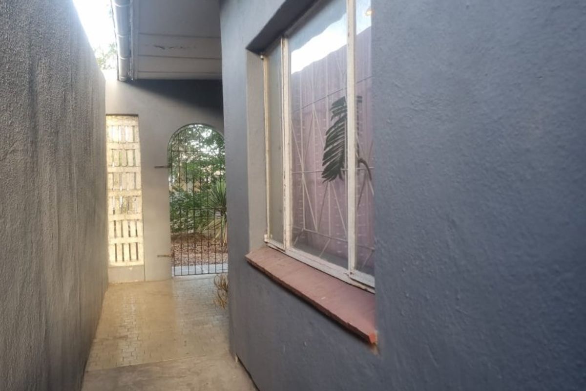 A side passage of the house featuring a concrete walkway, a metal-framed window with a security gate, and a glass brick accent wall.
