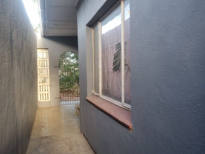 A side passage of the house featuring a concrete walkway, a metal-framed window with a security gate, and a glass brick accent wall.