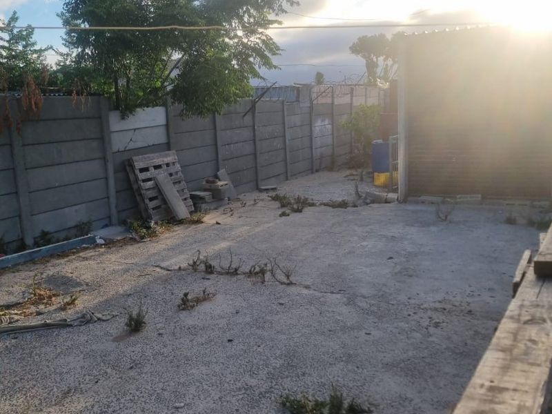 A rear outdoor area featuring a concrete paved surface enclosed by a precast concrete boundary wall with security razor wire.