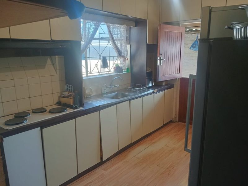 A functional kitchen featuring built-in cabinetry, an electric hob with extractor fan, and a stainless steel sink, with direct access to the exterior.