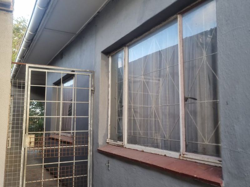 A view of the rear exterior wall featuring metal window frames with security bars and a metal security gate.