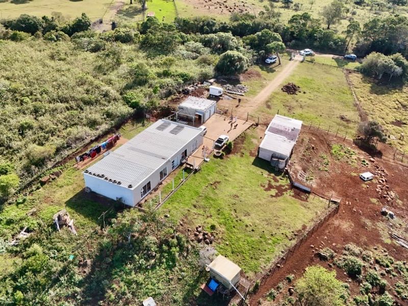 Aerial view of a farm property featuring a main dwelling, multiple outbuildings, fenced paddocks, and a gravel driveway set within a rural landscape.
