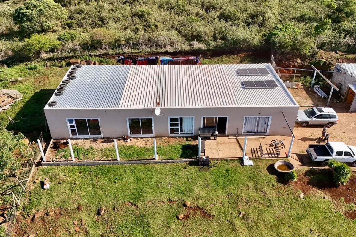 Aerial view of a single-story farm dwelling featuring a corrugated metal roof with solar panels, sliding glass doors, and an adjacent concrete patio area.