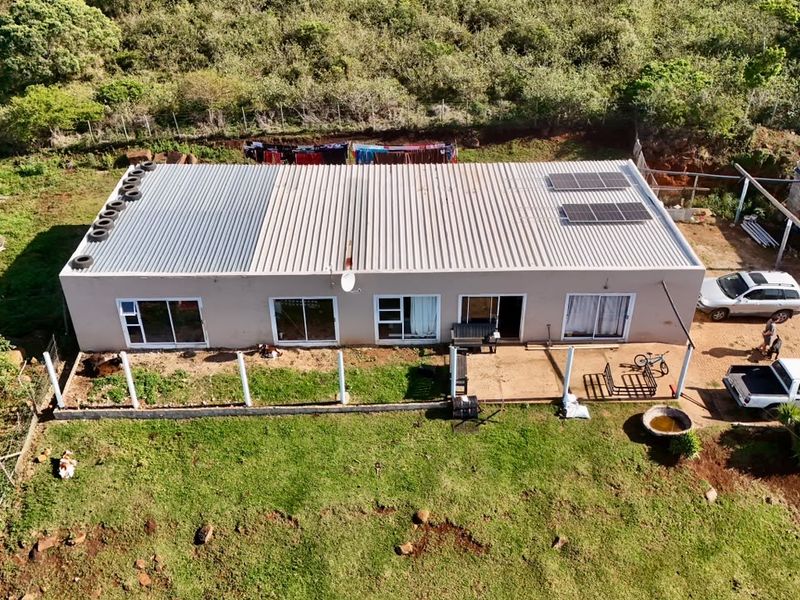 Aerial view of a single-story farm dwelling featuring a corrugated metal roof with solar panels, sliding glass doors, and an adjacent concrete patio area.