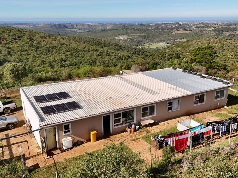 Aerial view of a rural property featuring a single-story dwelling with a corrugated metal roof, integrated solar panels, and expansive surrounding landscape.