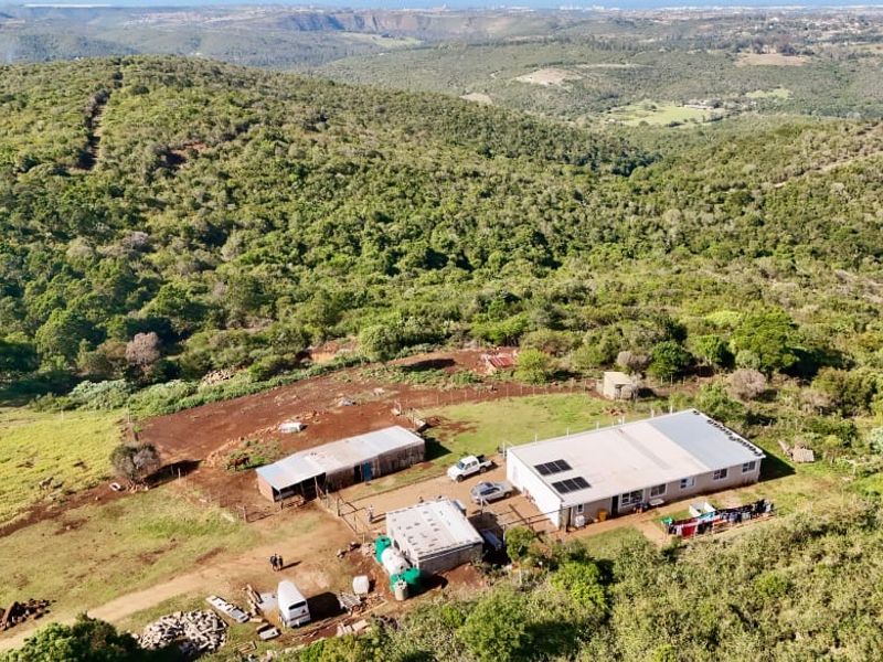 Aerial view of a rural farm property featuring a main dwelling with solar panels, multiple outbuildings, and surrounding natural landscape.
