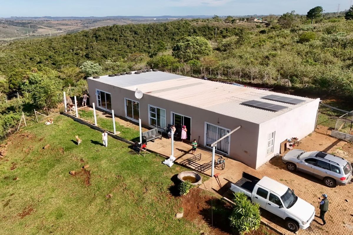 Aerial view of a single-story farm residence featuring a corrugated metal roof with solar panels, sliding glass doors, and an expansive surrounding landscape.