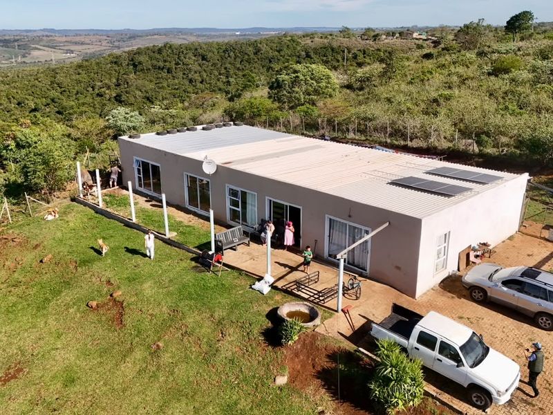 Aerial view of a single-story farm residence featuring a corrugated metal roof with solar panels, sliding glass doors, and an expansive surrounding landscape.