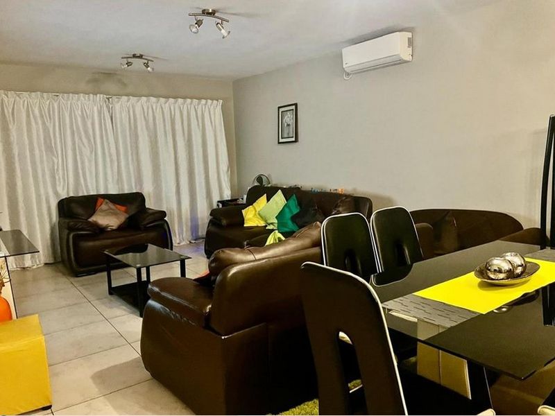 Open-plan living and dining area featuring tiled flooring, track lighting, and a wall-mounted split-system air conditioner.