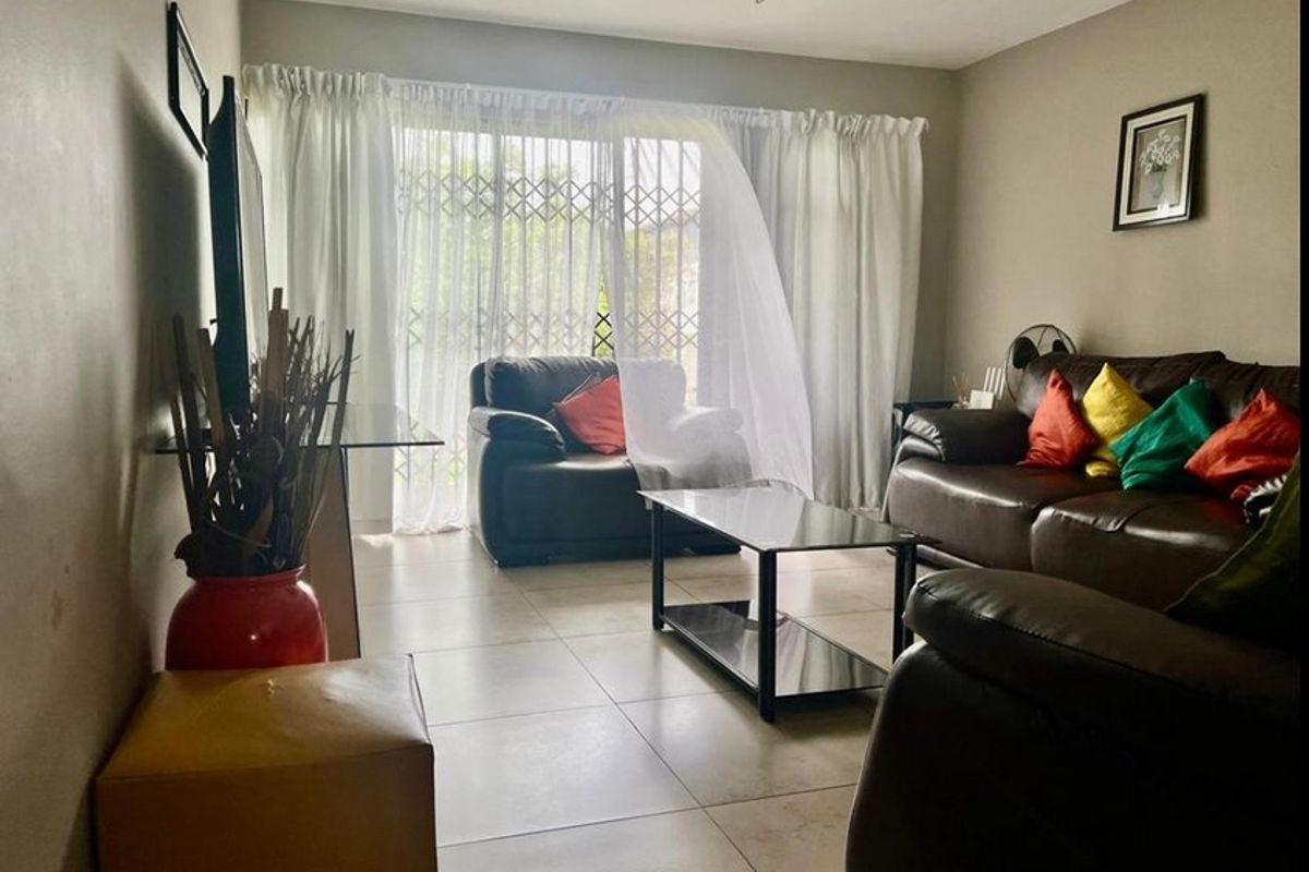A comfortable living room featuring tiled flooring and a sliding glass door with a security gate, providing access to the outdoor area.