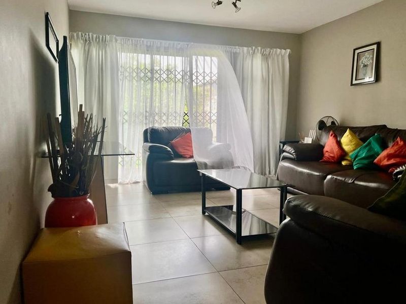 A comfortable living room featuring tiled flooring and a sliding glass door with a security gate, providing access to the outdoor area.