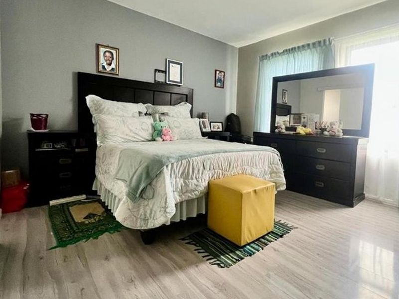 A well-lit bedroom featuring light-toned laminate flooring and neutral grey wall paint, providing a clean and functional space.