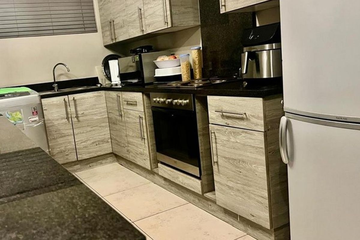 A functional kitchen featuring wood-look cabinetry, dark granite countertops, integrated oven and hob, and tiled flooring.