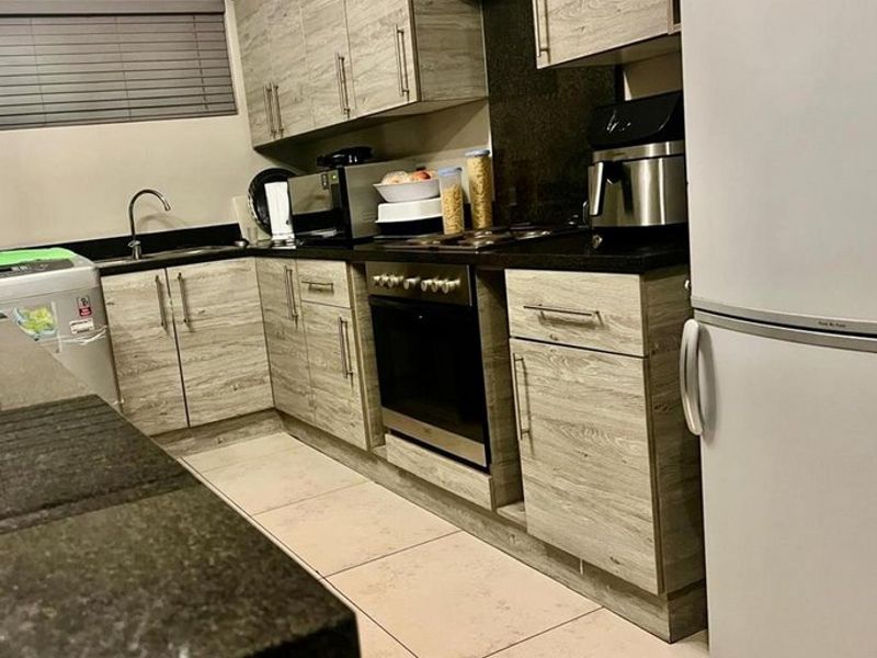 A functional kitchen featuring wood-look cabinetry, dark granite countertops, integrated oven and hob, and tiled flooring.