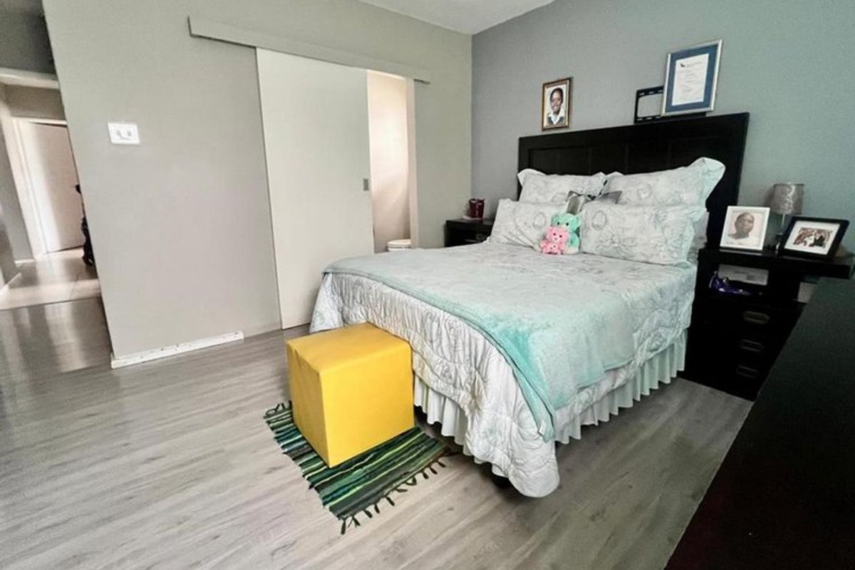 A well-maintained bedroom featuring light-toned laminate flooring and a functional sliding door leading to an adjacent space.