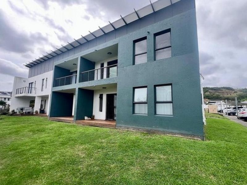 Rear view of a modern apartment building featuring private balconies with timber decking, metal railings, and a shared lawn area.