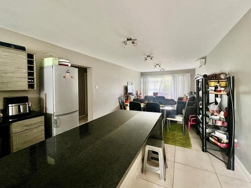 Open-plan living area featuring a kitchen with a granite island, tiled flooring, and direct access to the patio through sliding glass doors.