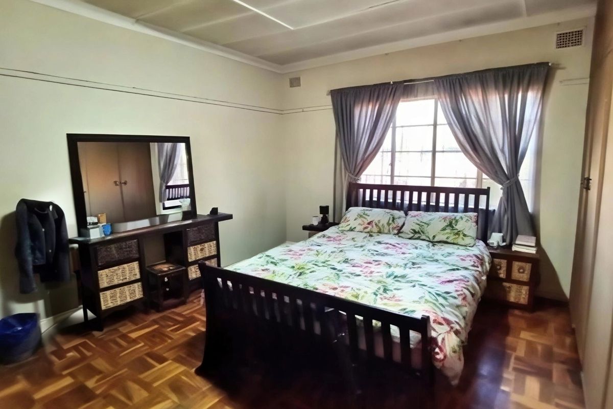 A well-proportioned bedroom featuring classic parquet flooring, built-in storage cupboards, and natural light through a steel-framed window.