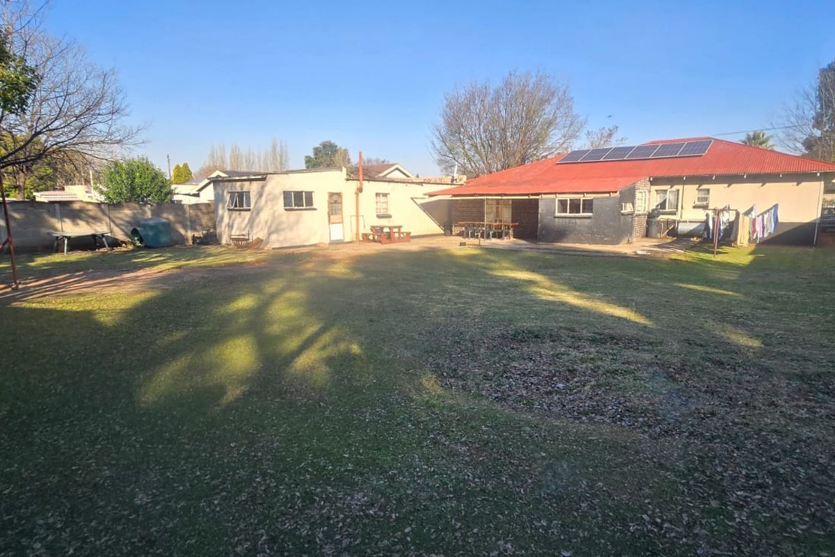 Spacious rear garden featuring a large lawn, paved patio area, and a house with a metal roof and installed solar panels.