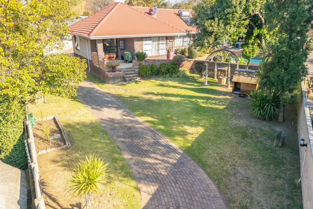 Aerial view of a brick house featuring a paved driveway, landscaped garden, and a swimming pool in the rear.